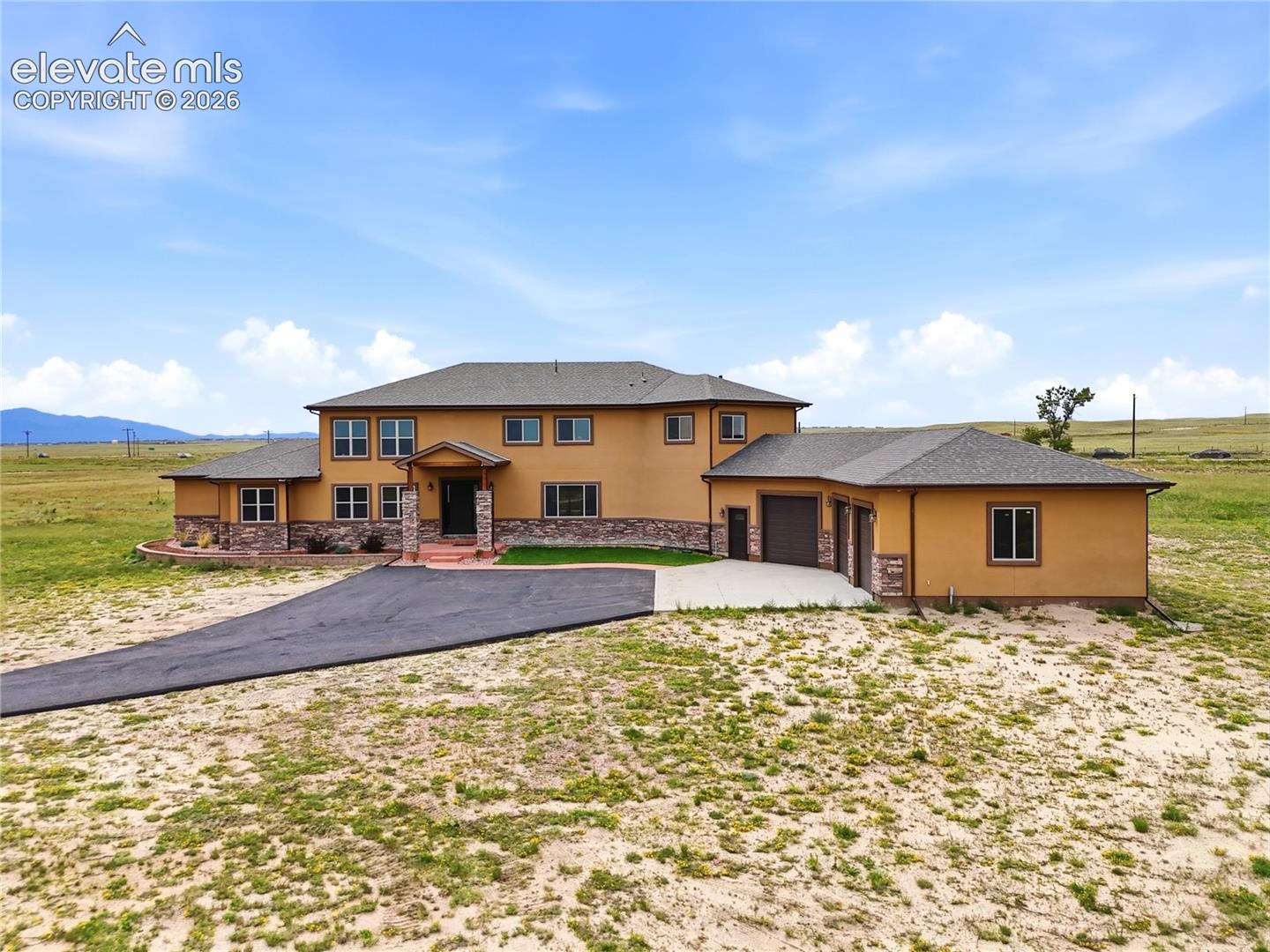 Exterior featuring stucco finish, stone accents, multiple windows, a paved driveway, and an attached two-car garage