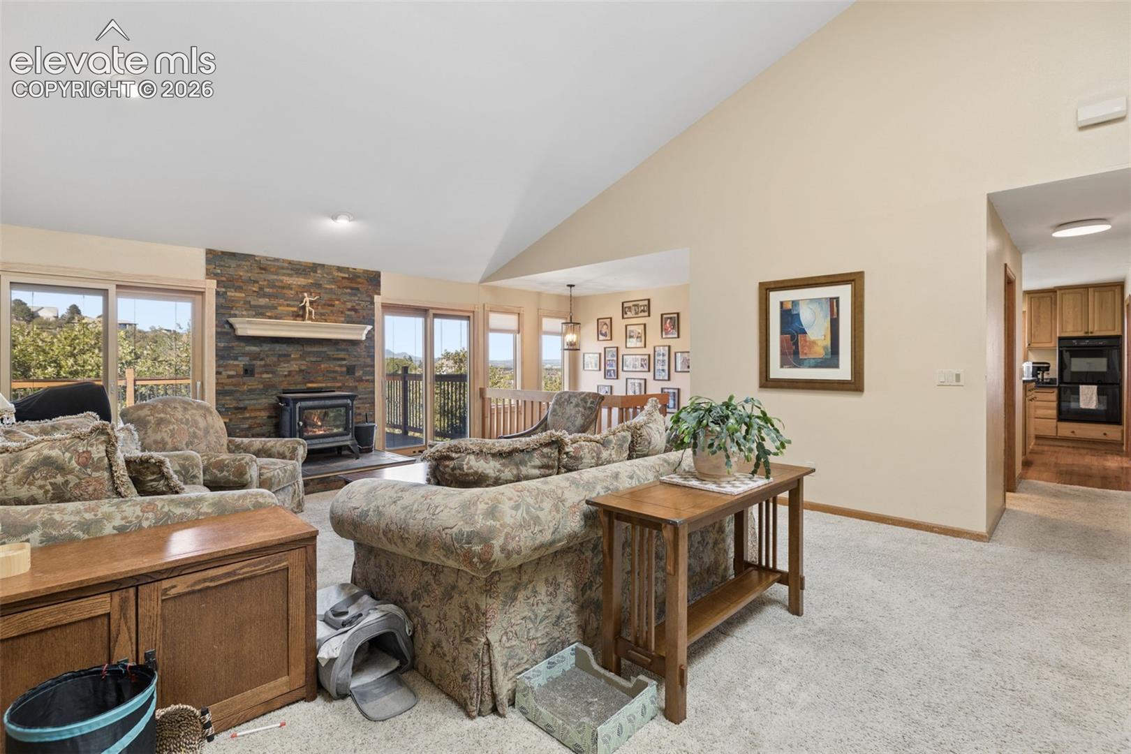 Vaulted ceilings, stone-finish fireplace surround, wood-mantel shelf, inset wood-burning stove, and glass sliding doors