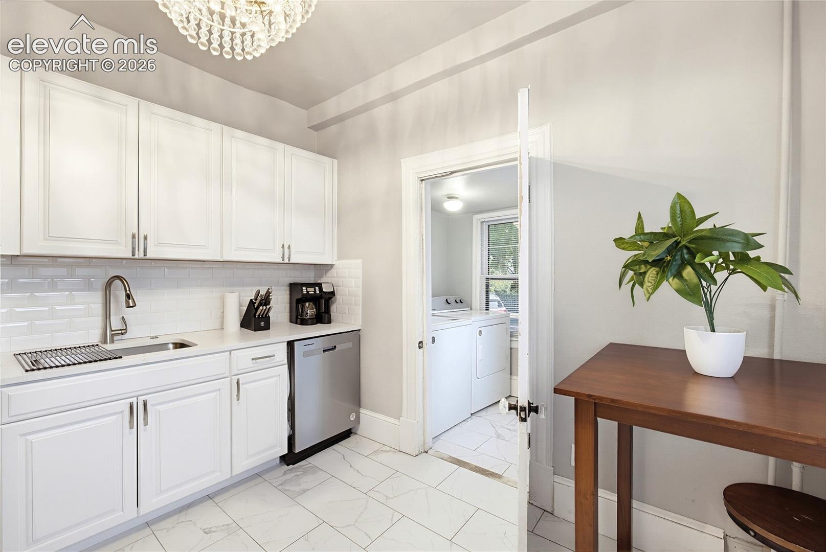 Kitchen featuring white cabinetry, subway tile backsplash, stainless steel dishwasher, and a crystal chandelier