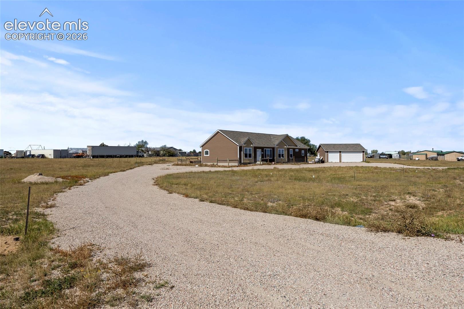 Single-story residence featuring vinyl siding, a gabled roofline, an attached two-car garage, and a sprawling gravel driveway situated on a large open lot