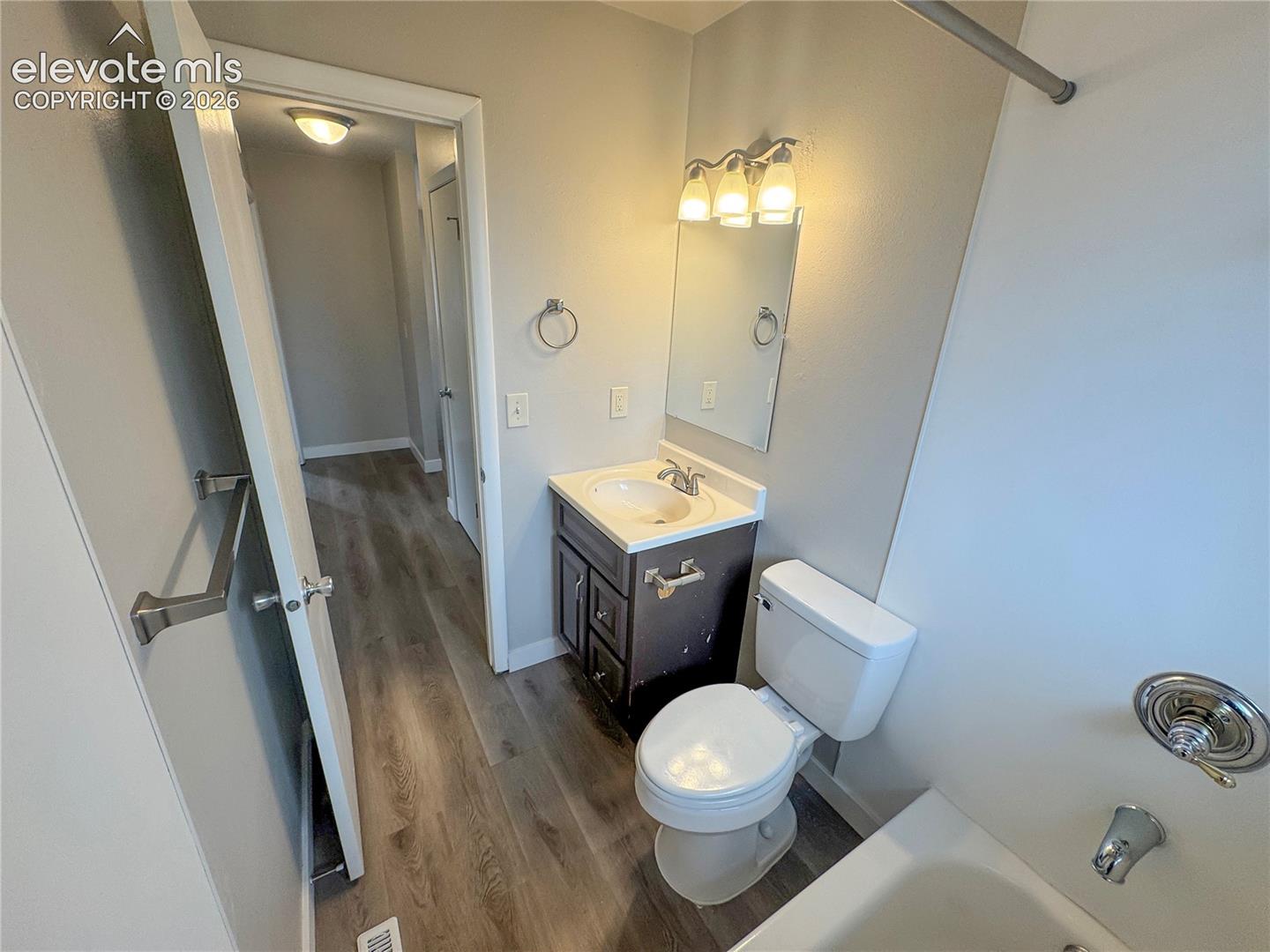 Bathroom featuring a vanity with a white integrated sink, three-light vanity fixture, mirror, and wood-finish flooring