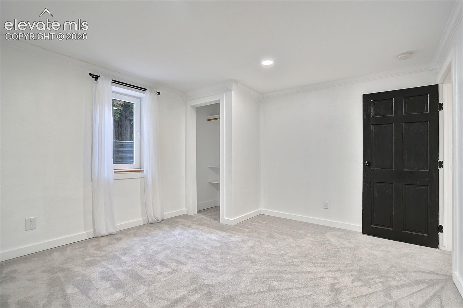 Neutral carpeting, recessed lighting, crown molding, and a six-panel door with matte black hardware