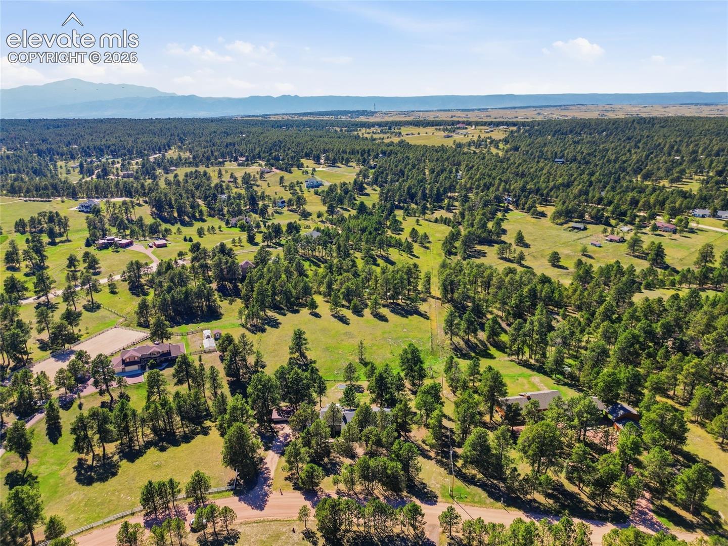 Expansive forested landscape featuring scattered residential structures, open grassy areas, and a distant mountain range