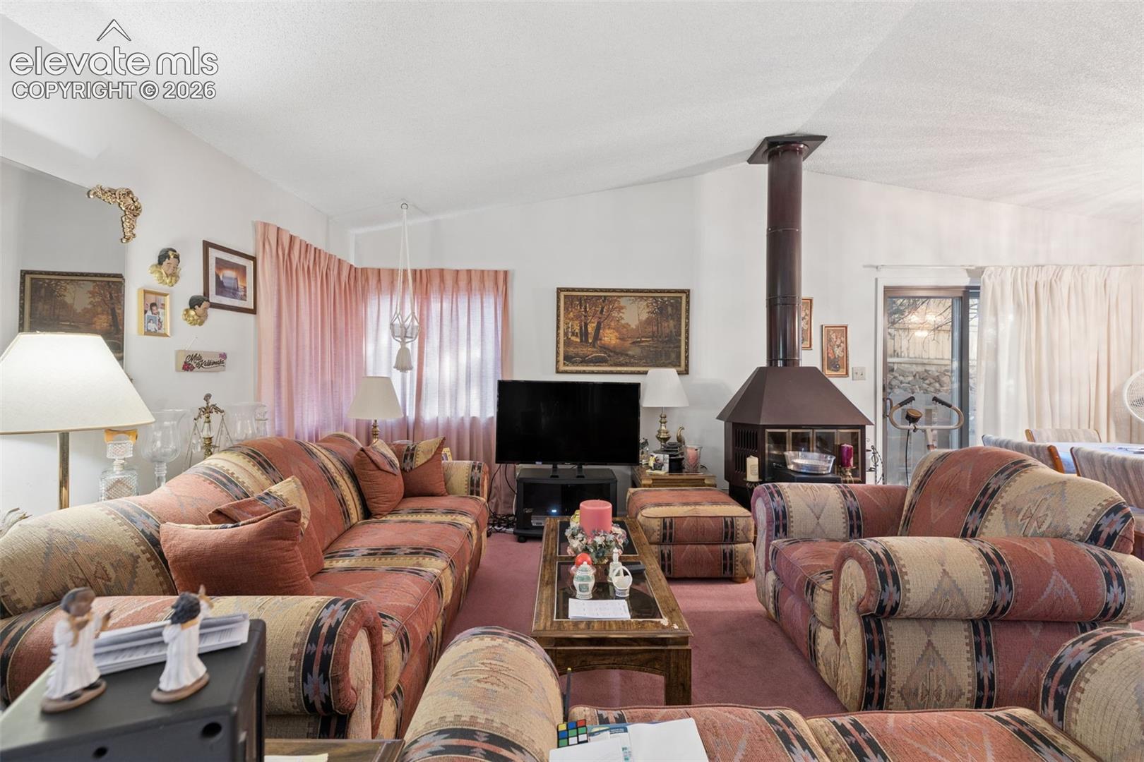Vaulted ceilings and a freestanding wood-burning fireplace with a chimney stack