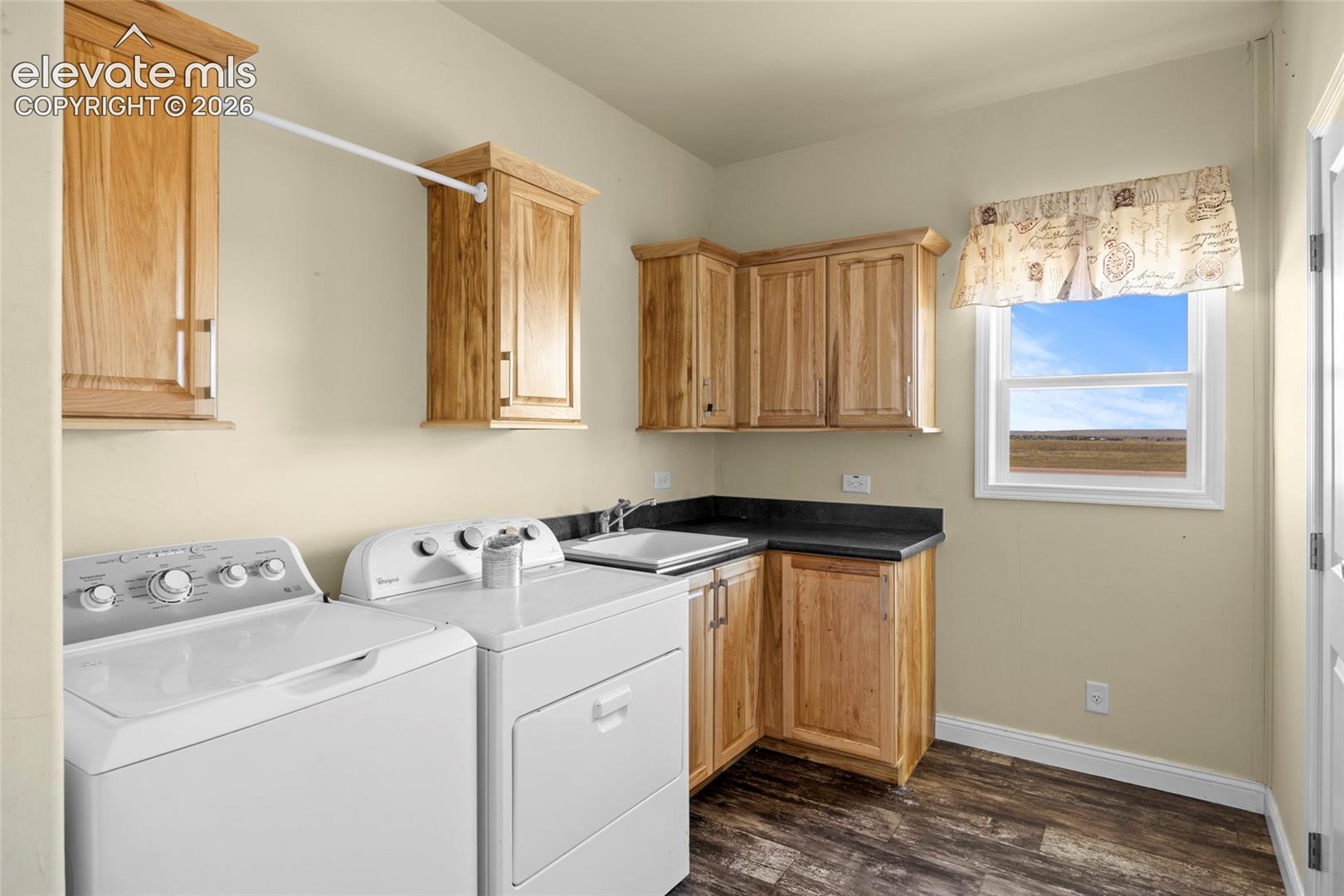 Laundry area featuring natural wood cabinetry, dark stone-finish countertops, an integrated utility sink with a chrome faucet, and wood-finish flooring