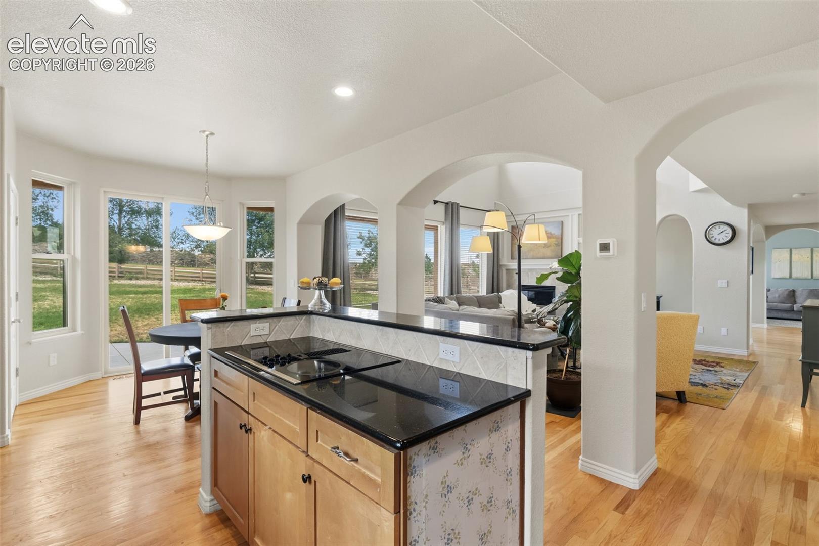 Kitchen island with black granite countertop, integrated cooktop, and light wood cabinetry