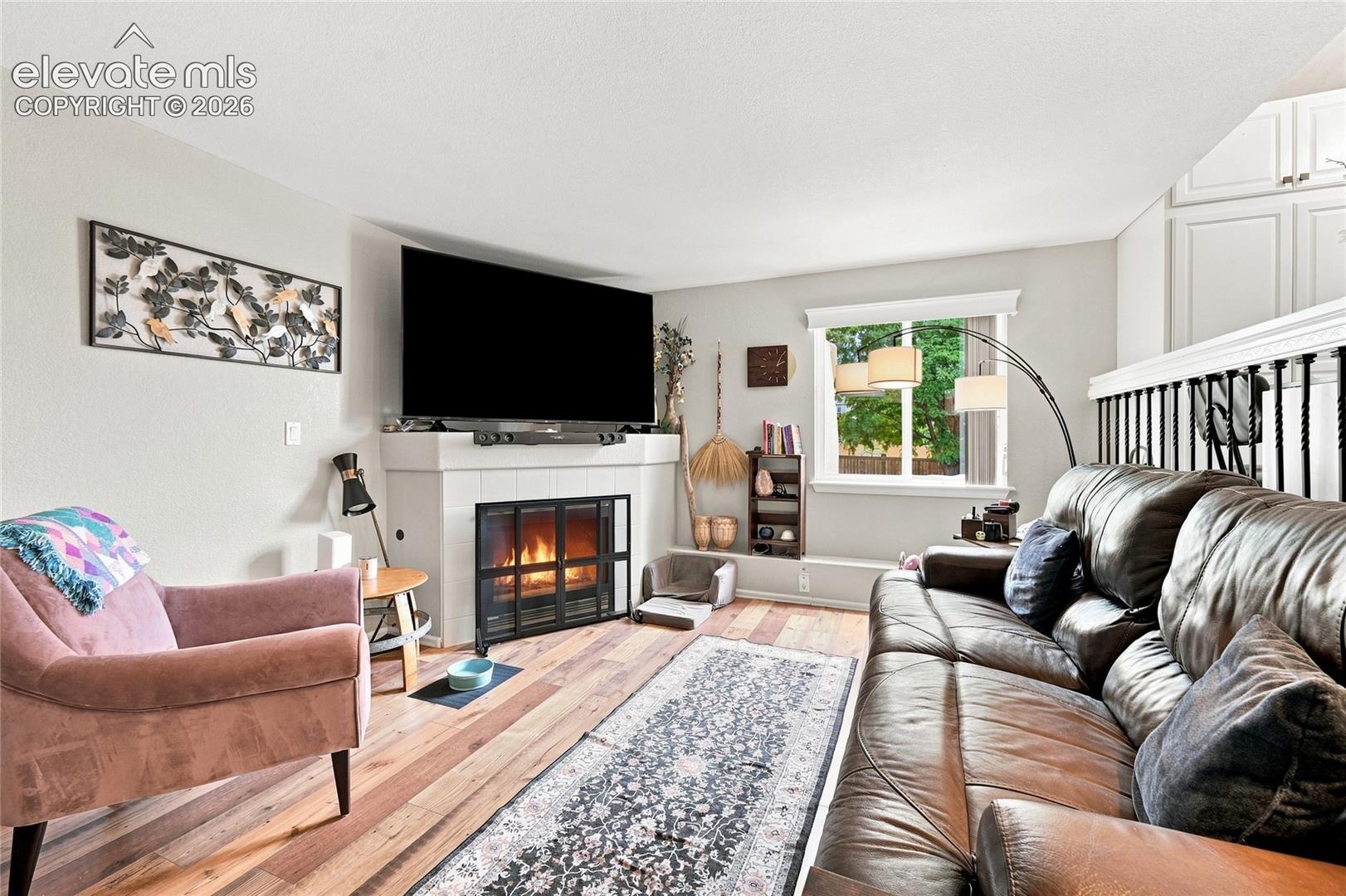 Fireplace with tile surround, wood-finish flooring, and white railing with black metal balusters