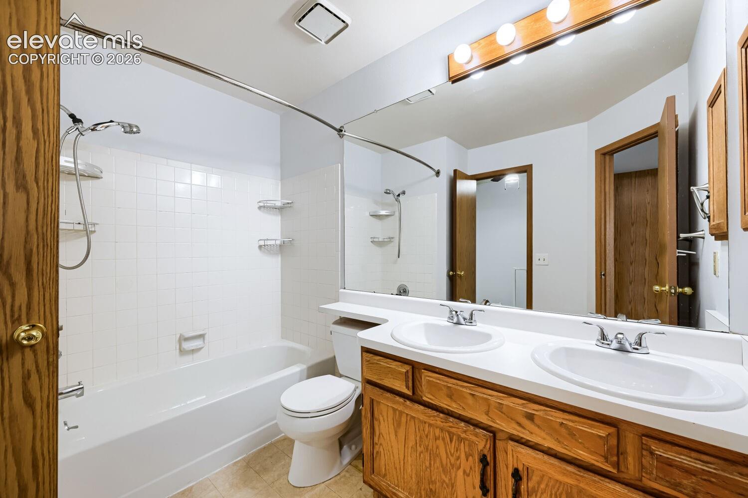 Bathroom featuring a dual vanity with white oval sinks, a built-in bathtub with white subway tile surround, wood-finish cabinetry, and a full-width mirror