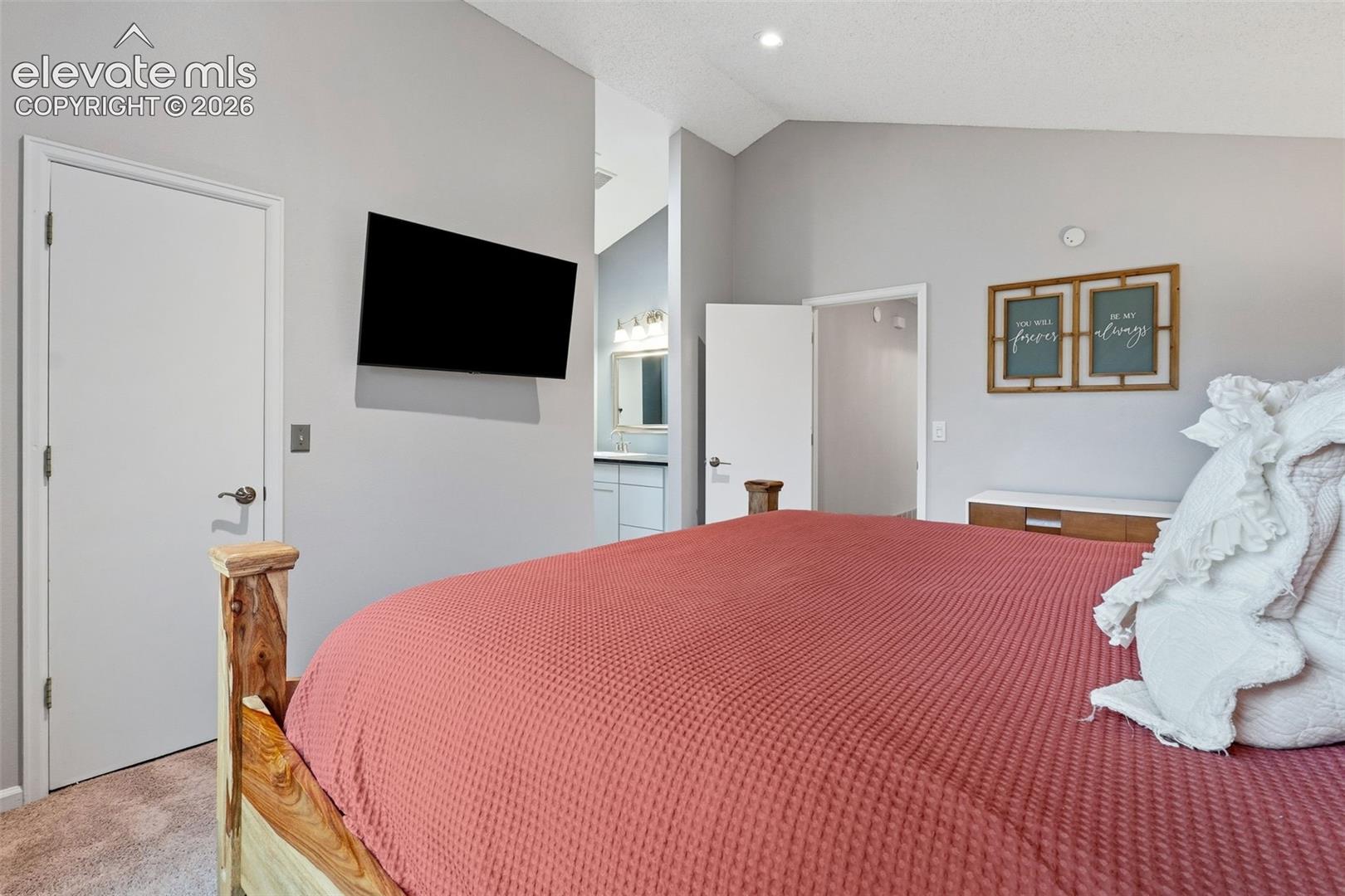 Vaulted ceiling, recessed lighting, wall-mounted television, and wood-finish door frames