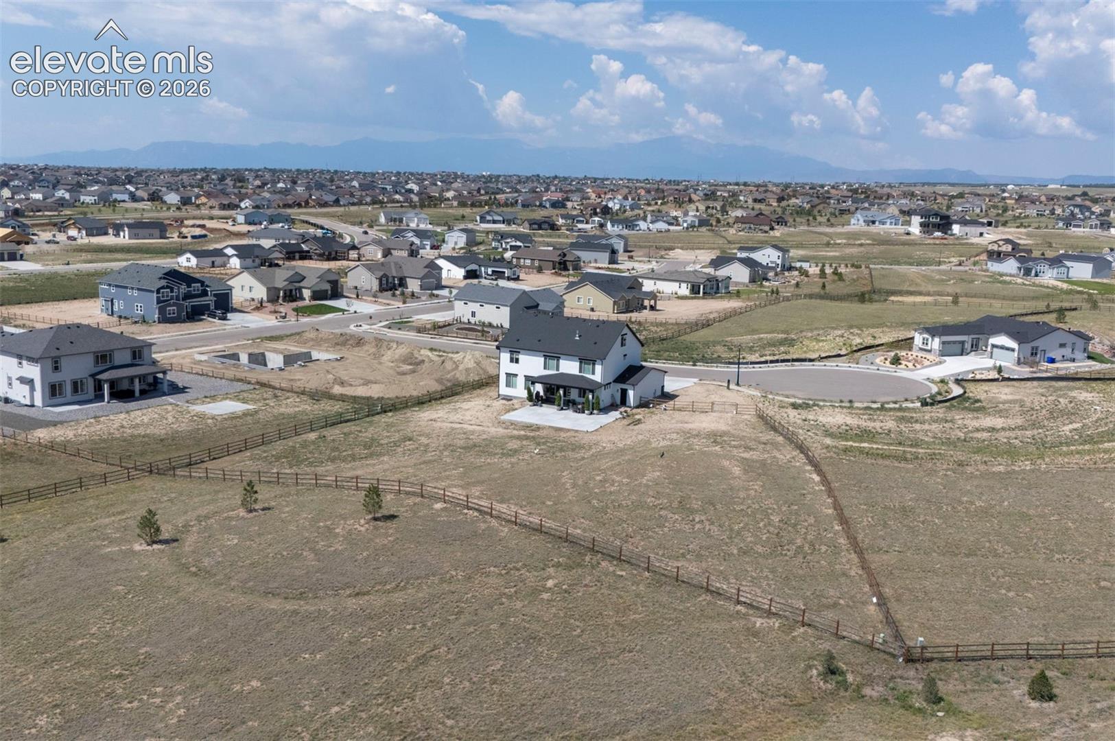 Spacious lot featuring perimeter fencing, several young trees, and a mountain backdrop