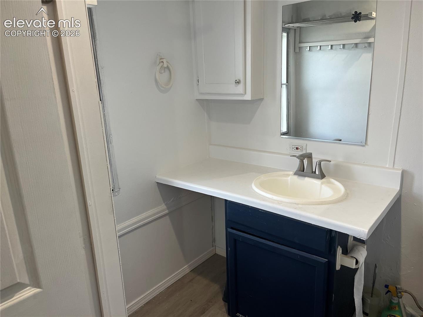 White vanity countertop with an integrated sink, blue-painted lower cabinetry, and a wall-mounted mirror