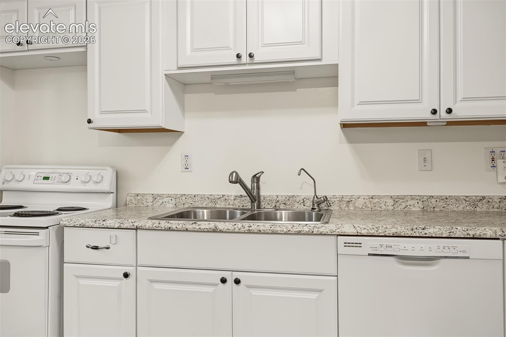 Kitchen featuring white shaker-style cabinetry, stone-finish countertops, stainless steel double-basin sink with pull-down faucet, and integrated dishwasher