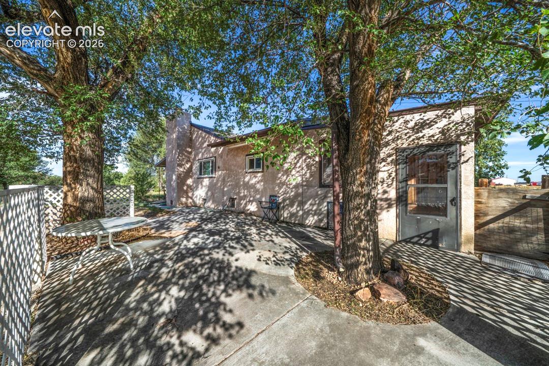 Stucco exterior with concrete patio, white lattice fencing, and mature trees