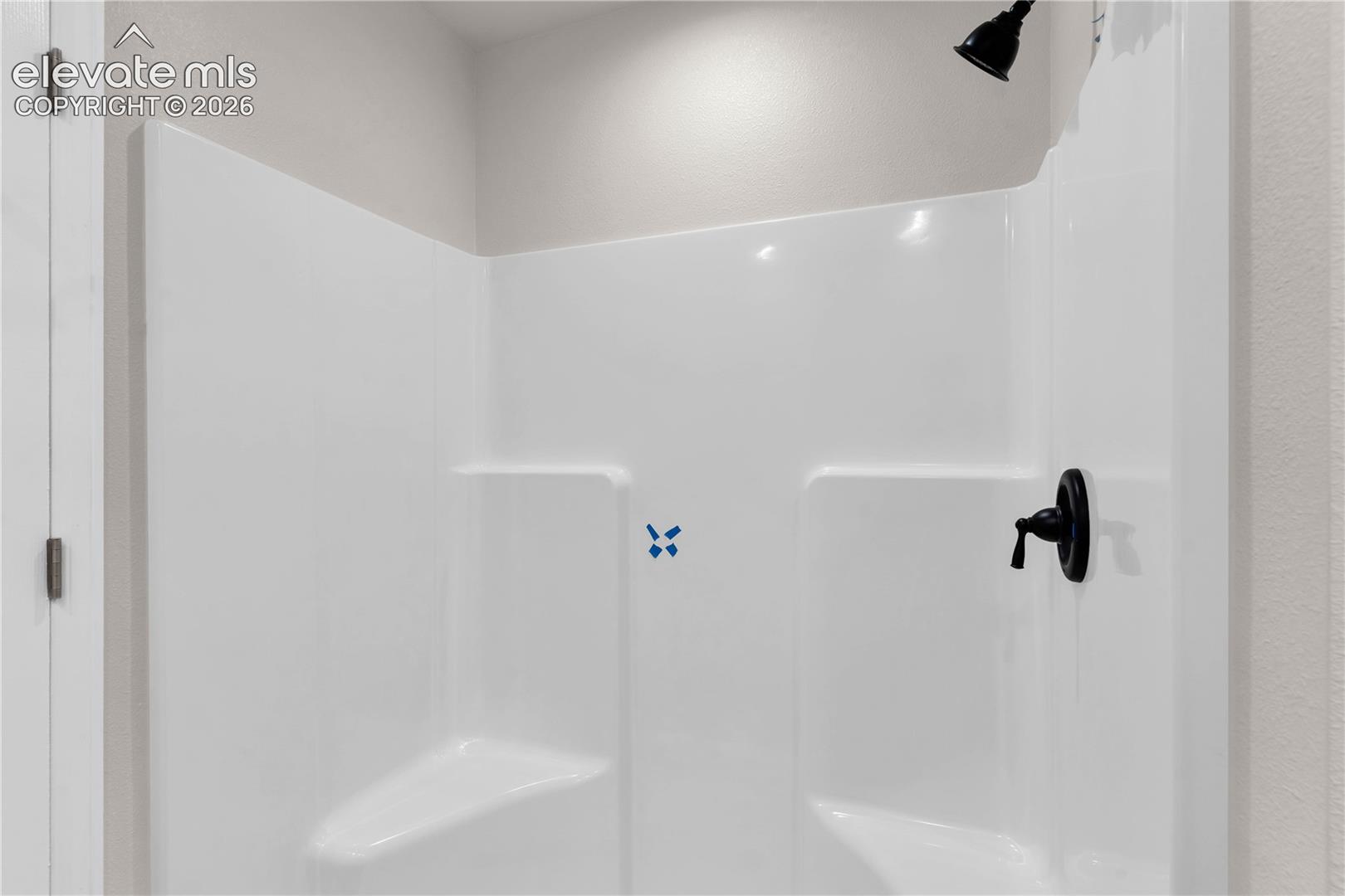 Shower enclosure featuring white molded walls, built-in corner shelving, and matte black plumbing fixtures