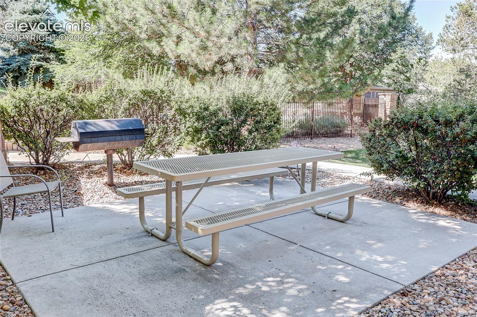 Concrete patio featuring a built-in metal grill and landscaping consisting of mature shrubs and trees