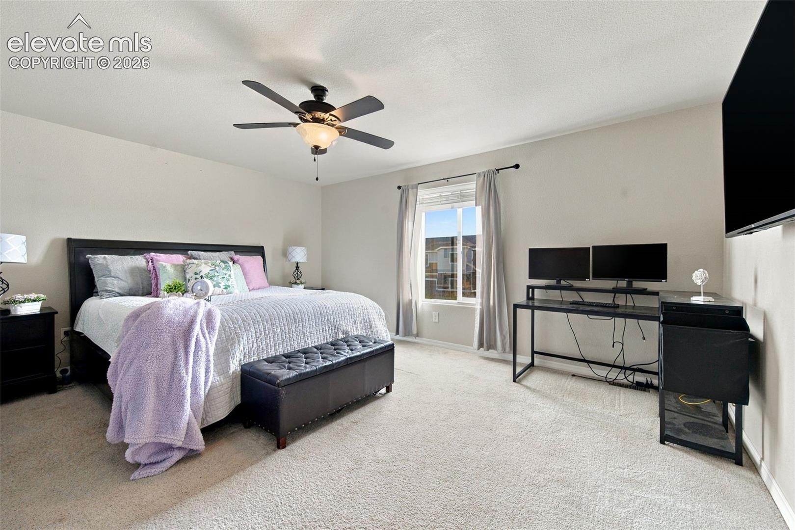 Bedroom featuring neutral-toned carpeting, a central ceiling fan with integrated lighting, and a window with a curtain rod