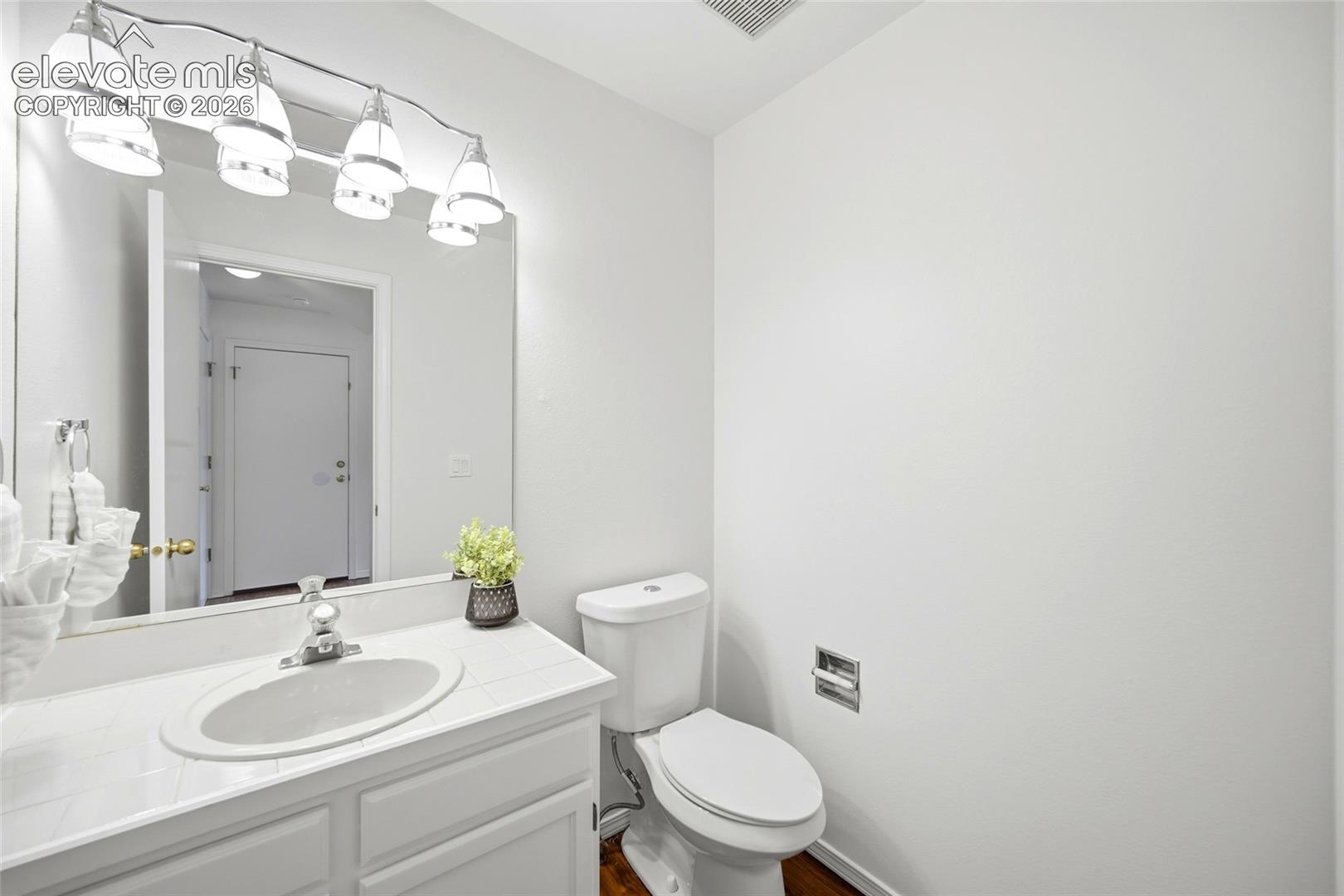 Bathroom featuring a tile-topped vanity with an integrated basin, chrome-finish faucet, wall-to-wall mirror, four-light vanity fixture, and a standard-height toilet