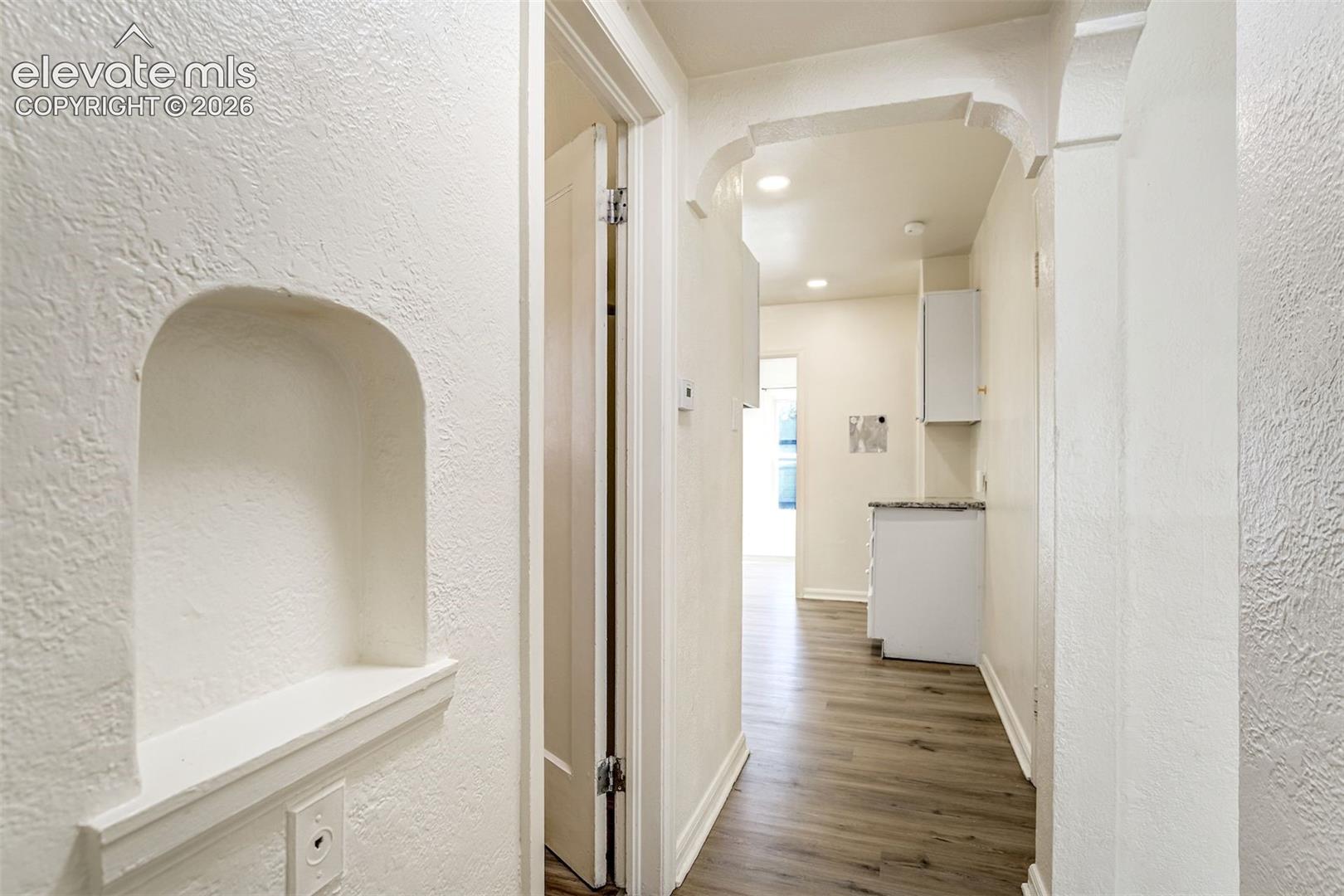 Interior corridor featuring an arched wall niche, recessed ceiling lighting, textured wall finish, and wood-finish flooring