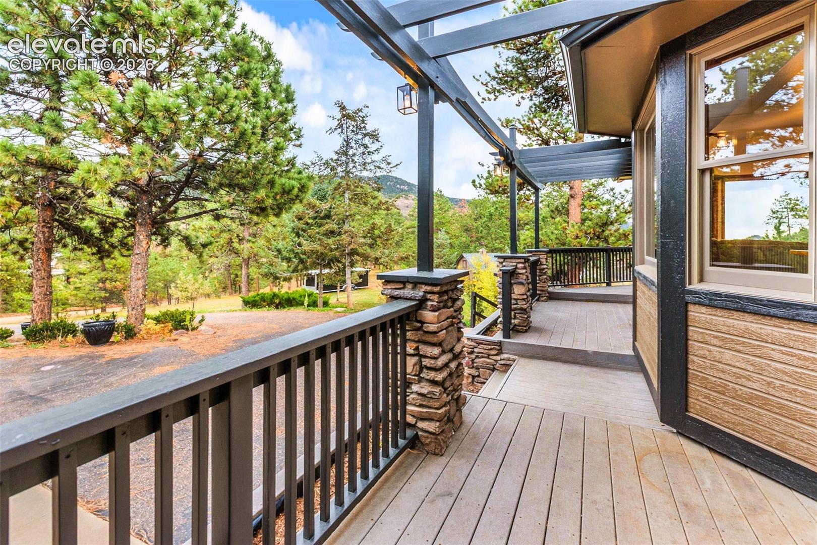 Wrap-around deck featuring tiered stone pillar supports, a dark metal pergola structure, and horizontal balustrades