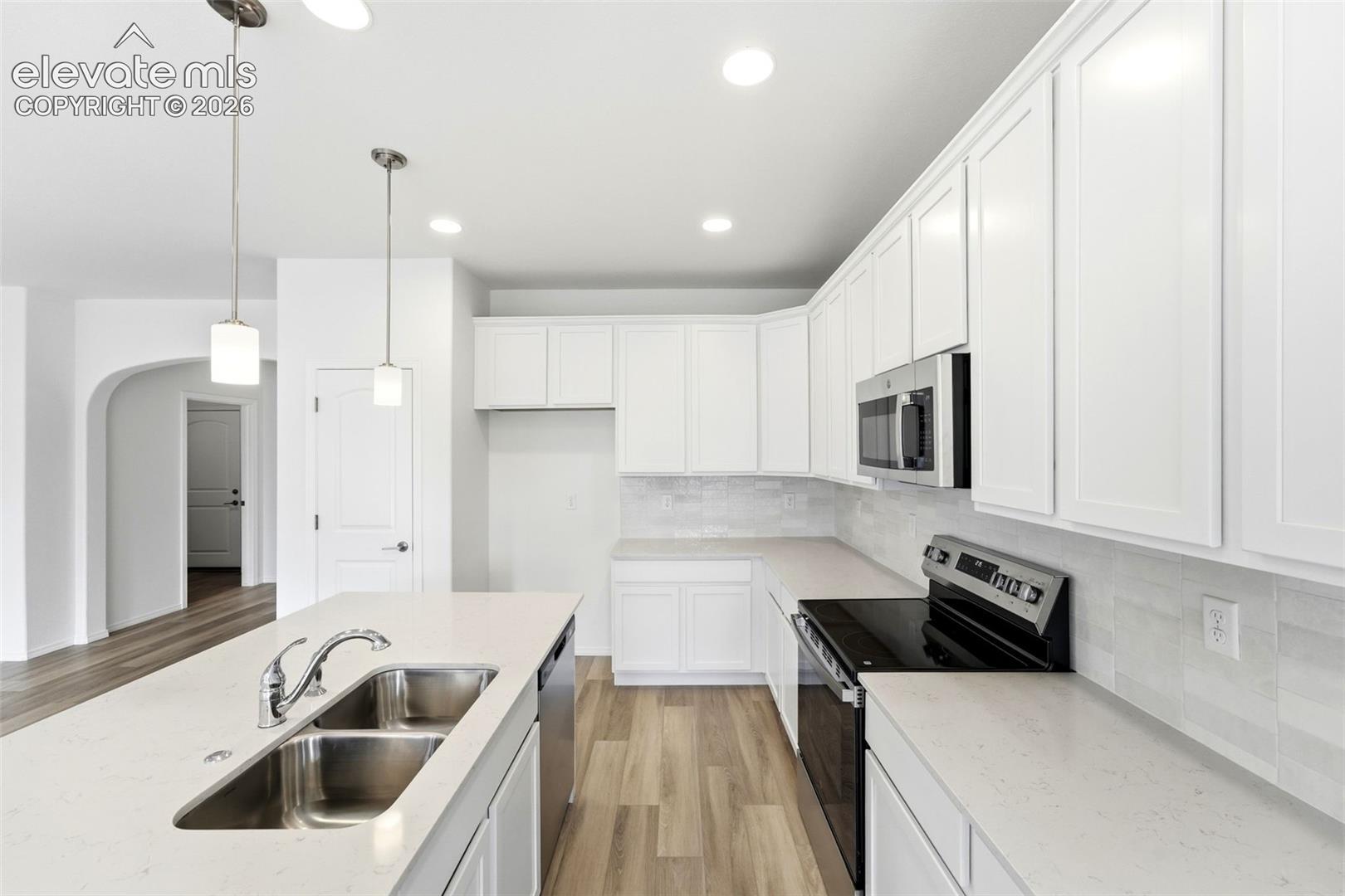 Kitchen featuring white shaker-style cabinetry, solid-surface countertops, wood-finish flooring, a stainless steel double-basin sink with a gooseneck faucet, and recessed lighting
