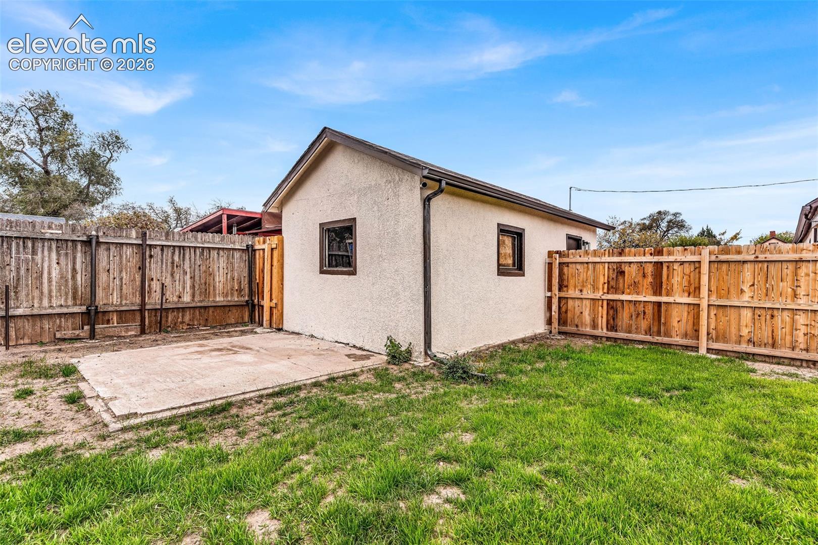 Detached exterior structure featuring stucco siding, a concrete pad, and a full wood-plank privacy fence