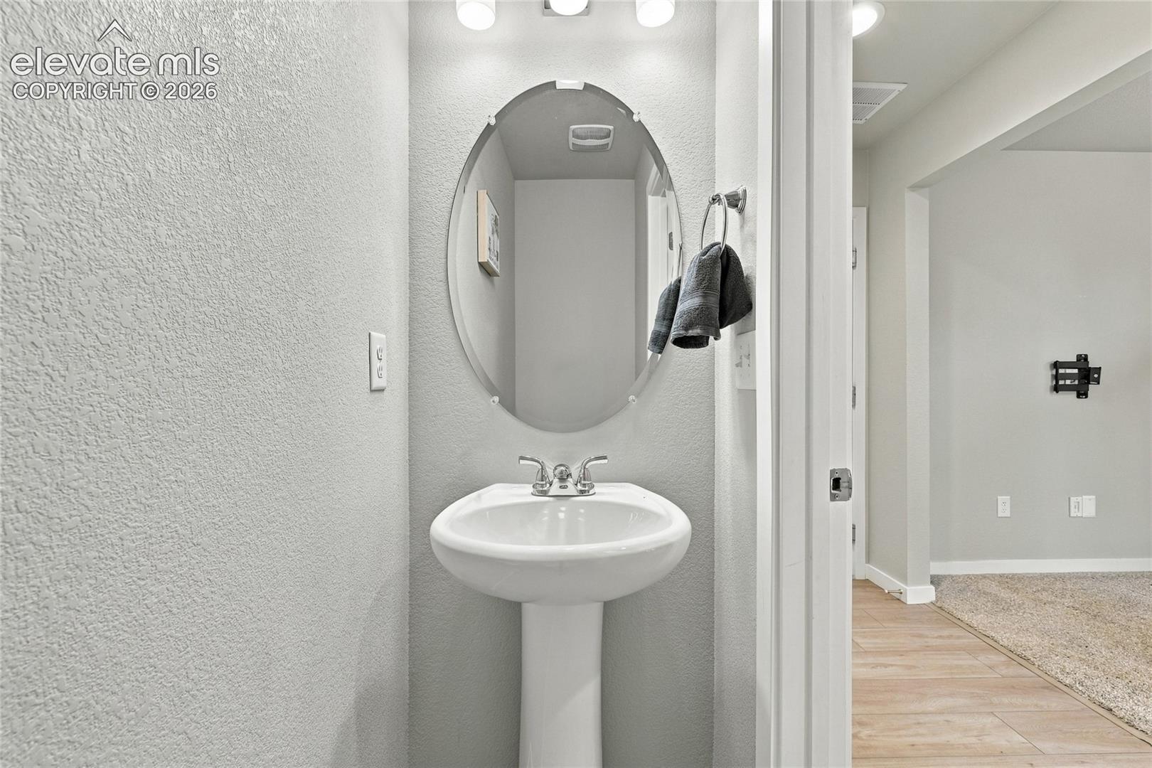 Pedestal sink with chrome faucet, an oval mirror, and wall-mounted lighting