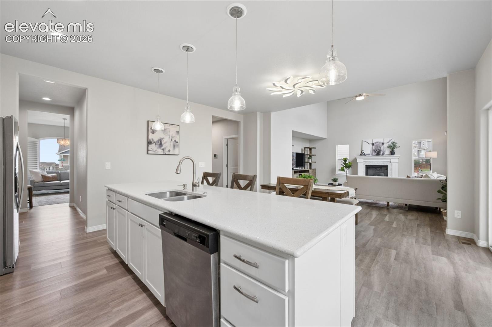 Open-concept kitchen and living area featuring a large center island with integrated sink, stainless steel dishwasher, and pendant lighting