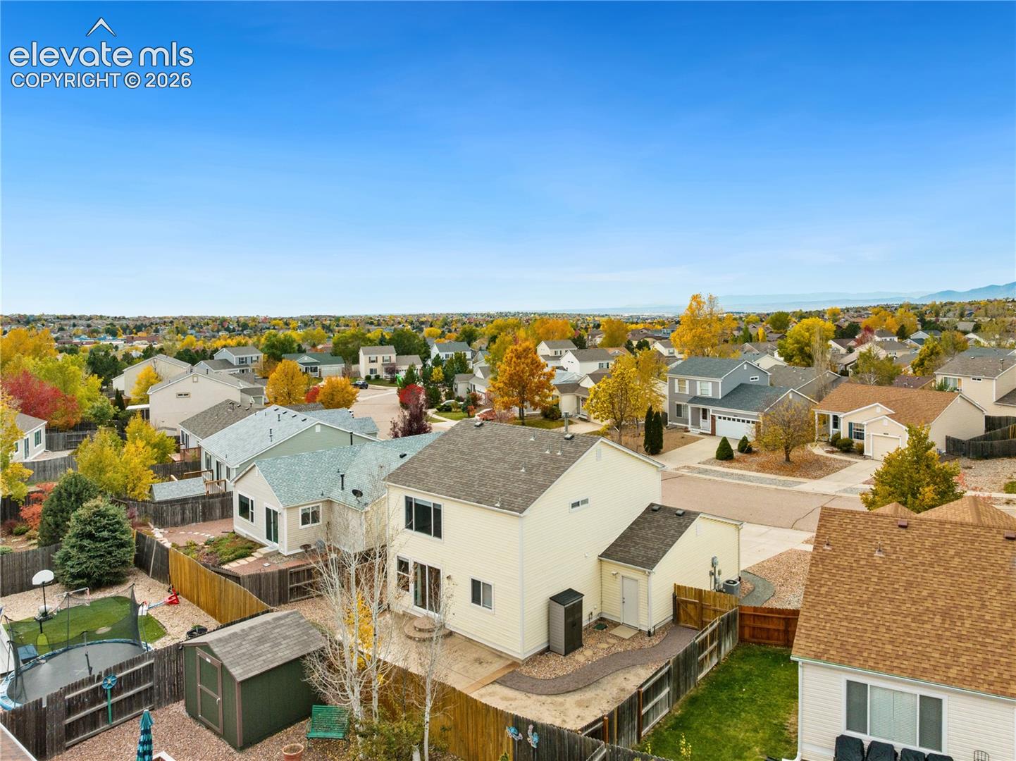 Aerial perspective featuring two-story residence with light-colored siding, asphalt shingle roof, rear concrete patio, and fenced perimeter