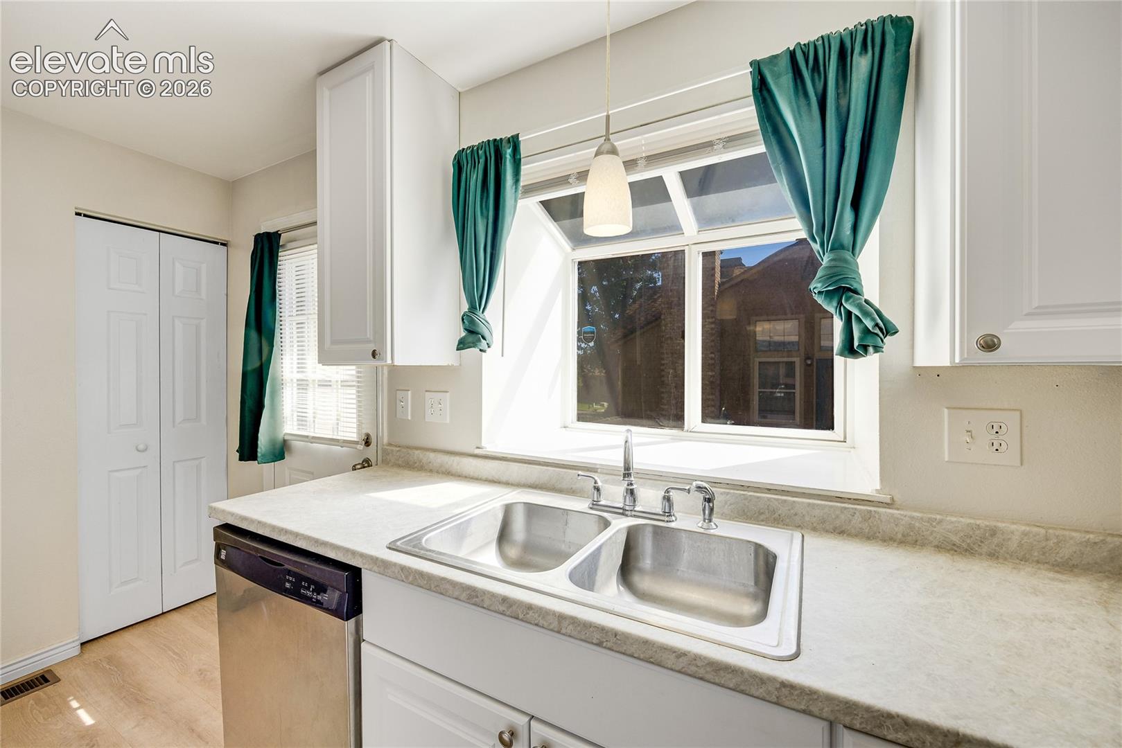 White cabinetry, stainless steel sink, light-toned countertops, stainless steel dishwasher, and wood-finish flooring