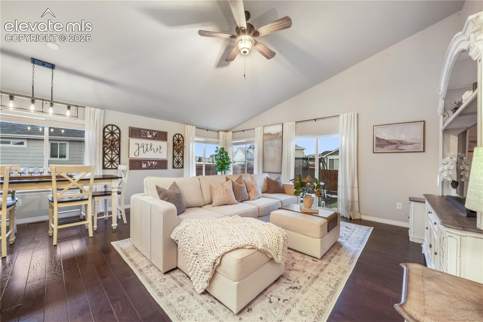 Vaulted ceiling with an attached ceiling fan, rich wood-finish flooring, and multiple large windows