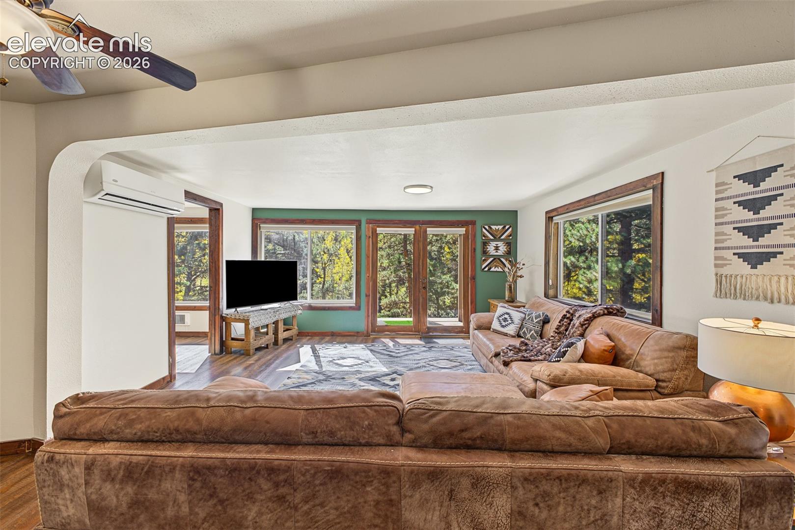 Spacious living area featuring wood-finish flooring, an arched doorway, and multiple large windows with wood trim