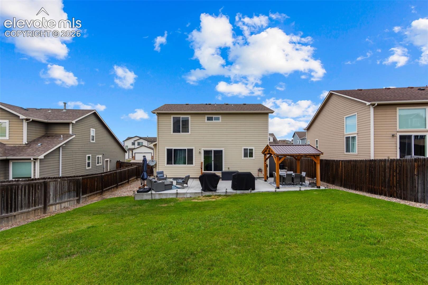 Expansive backyard featuring a large concrete patio, a built-in pergola, and mature fencing