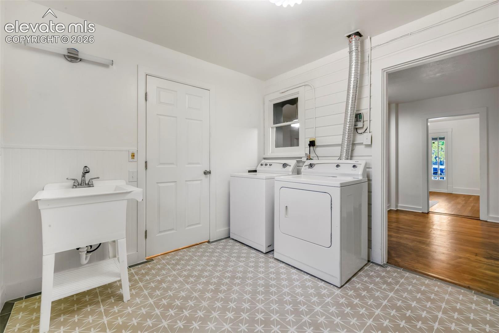 Laundry area featuring patterned tile flooring, shiplap wall accents, beadboard wainscoting, and a utility sink with a chrome faucet