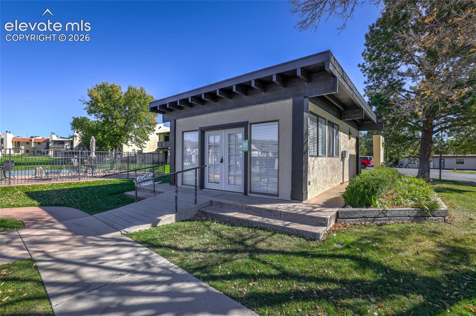 Detached structure featuring a low-slope roof with exposed rafters, stucco exterior, glass-pane double entry doors, and a concrete ramp with a metal handrail