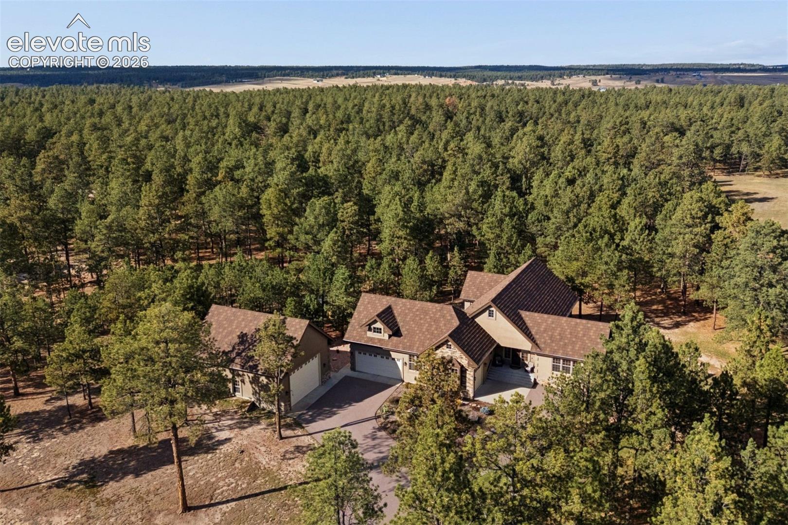 Residential estate featuring a multi-gabled roofline, stone and stucco exterior, attached multi-car garage, and paved driveway, all situated on a forested lot