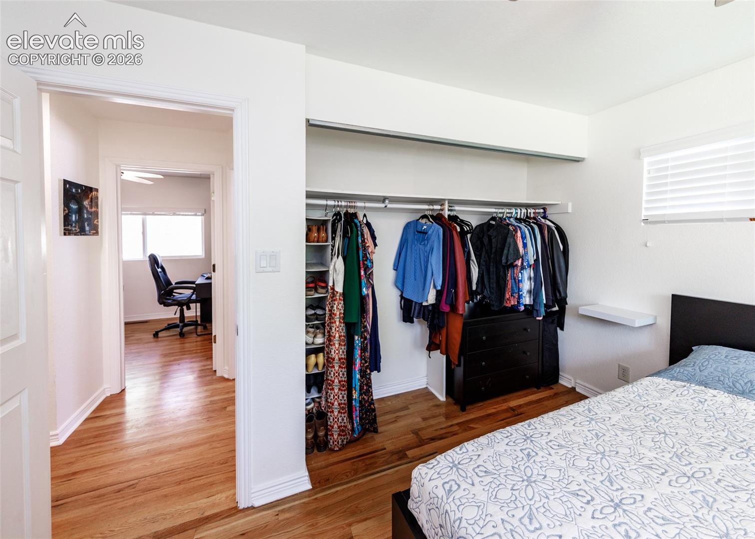 Hardwood flooring, open closet with built-in shelving, window with blinds, ceiling fan in adjoining room