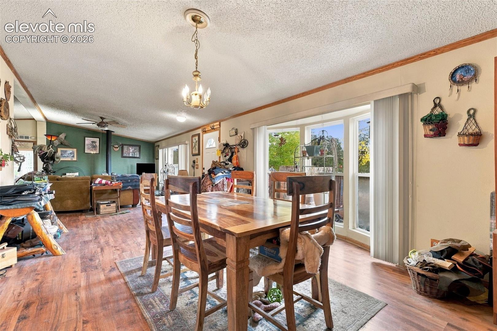 Open-concept interior featuring wood-finish flooring, a multi-paneled bay window, and a decorative ceiling-mounted chandelier