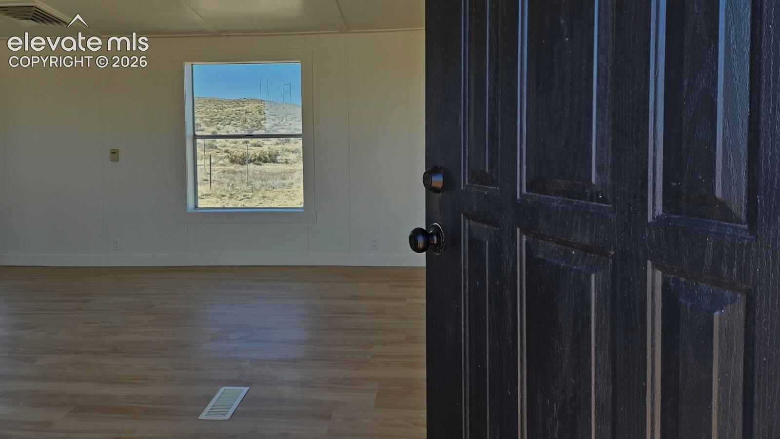 Dark-finished entry door with circular hardware, wood-finish flooring, and natural landscape scenery through a double-pane window