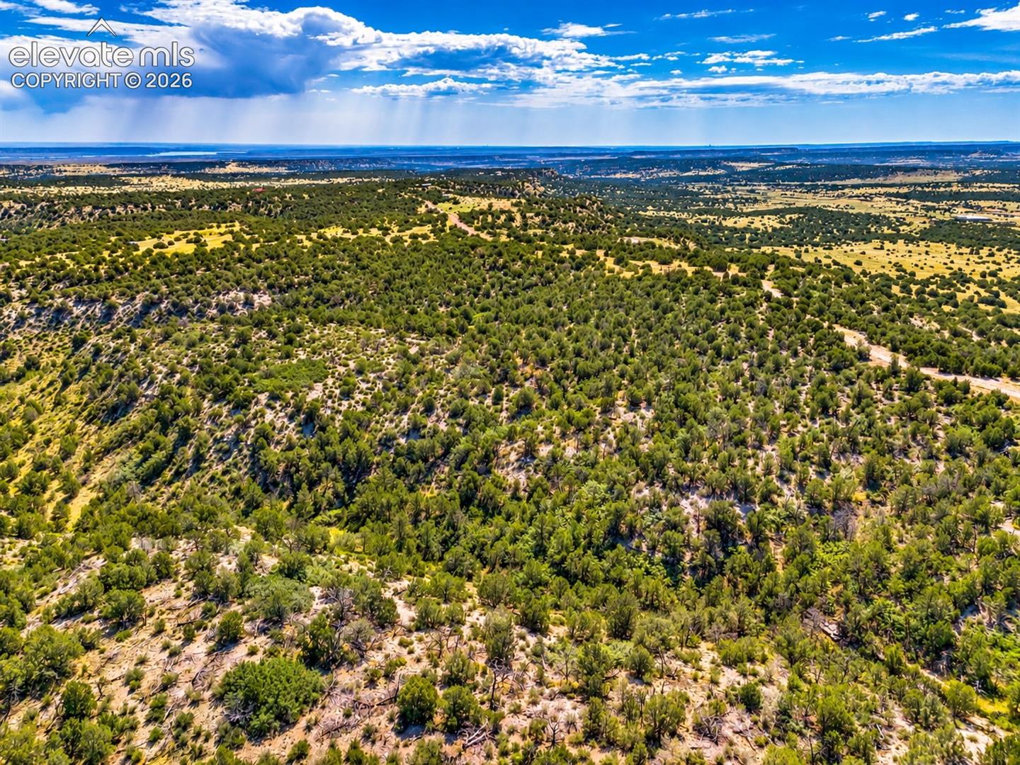 Beautiful aerial perspective of juniper-covered hillsides and natural terrain, surrounded by wide-open landscapes and distant mountain scenery.

