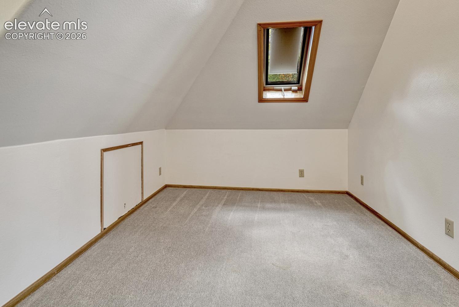 Carpeted attic space with a skylight and wood-trim access panel