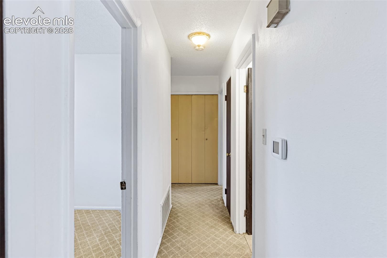 Bright hallway featuring clean white walls, neutral tile flooring with geometric pattern, and multiple doorways with wood-finish doors