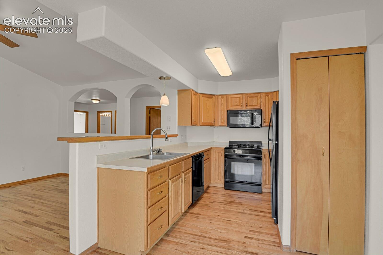 Kitchen featuring wood-finish flooring, light-toned cabinetry, a stainless steel sink, and black appliances