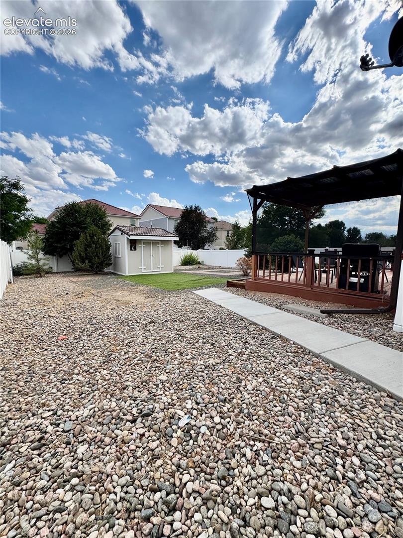 Expansive backyard featuring a large gravel area, a section of green lawn, and a white storage shed