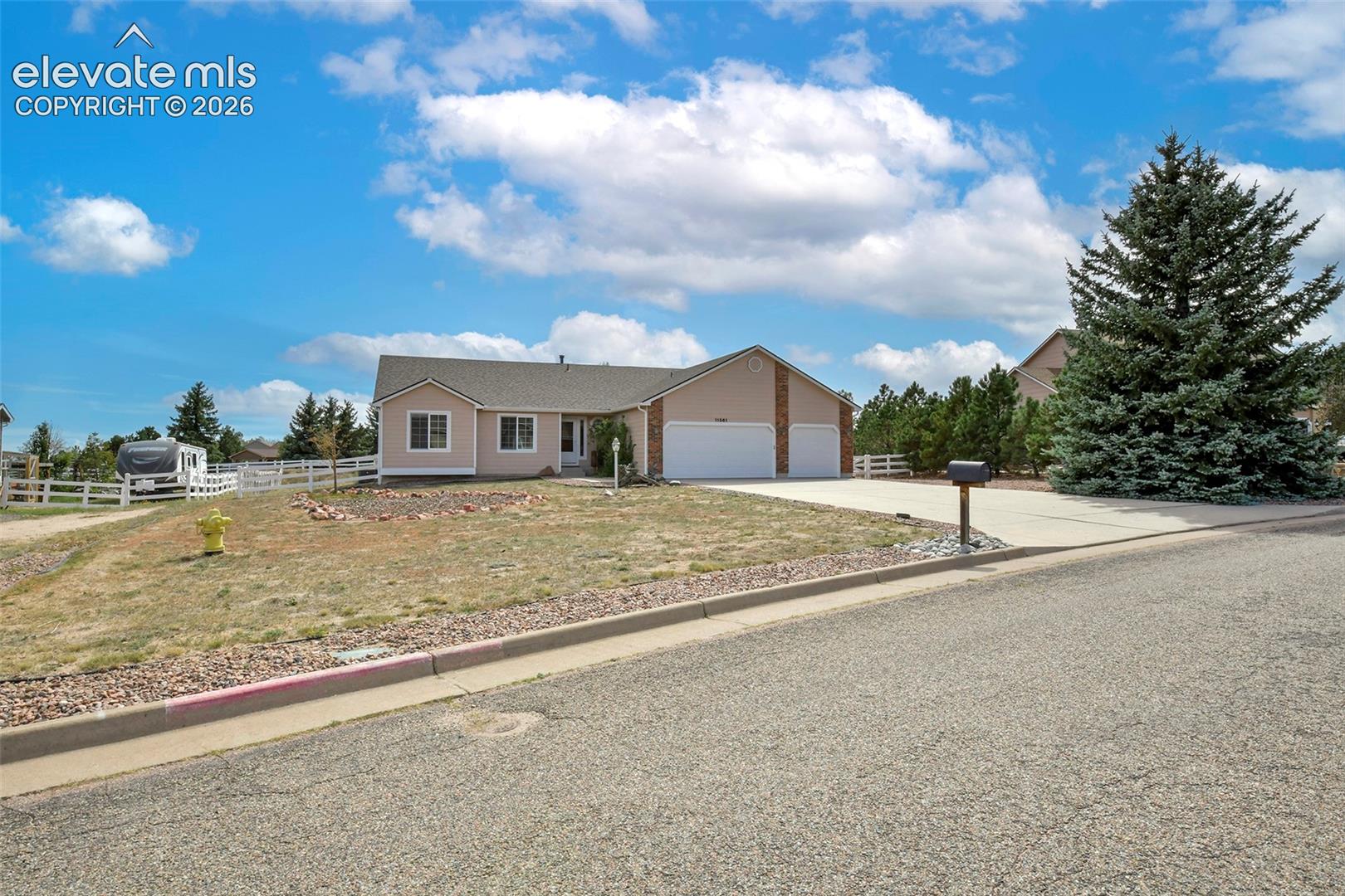 Ranch-style residence featuring a three-car garage, concrete driveway, and a mature evergreen tree