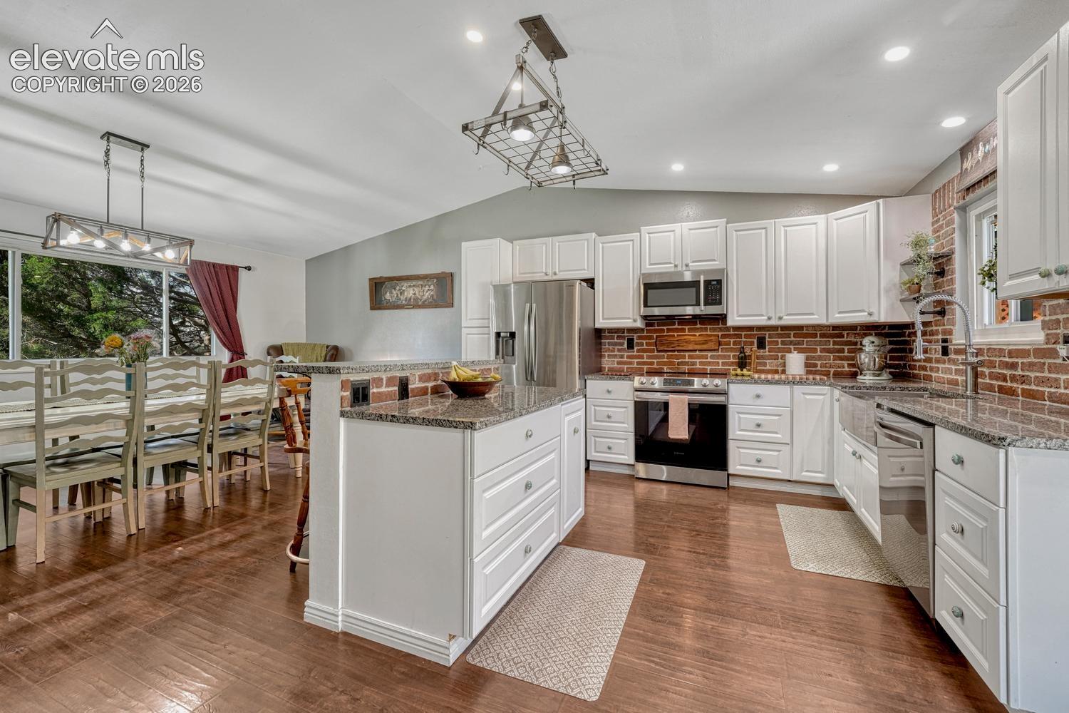 The updated Kitchen features white cabinetry, granite countertops, a brick backsplash, stainless steel farmhouse sink, breakfast bar, & stainless steel appliances.