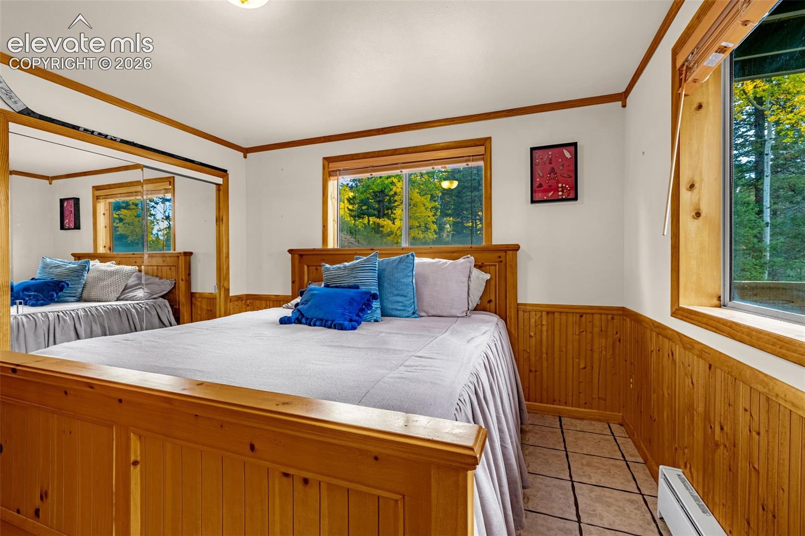 Wood-paneled wainscoting, sliding mirrored closet doors, tile flooring, and windows featuring exterior forest scenery