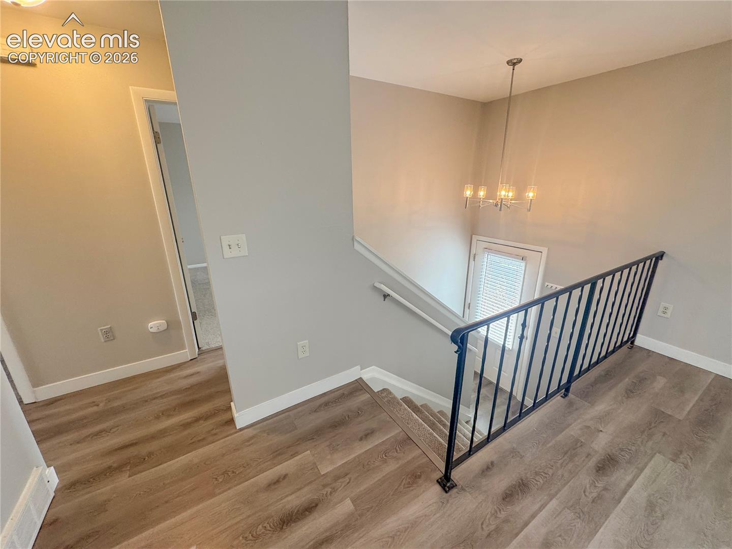 Stairwell featuring wood-finish flooring, black metal railing, neutral wall tones, and a multi-light chandelier