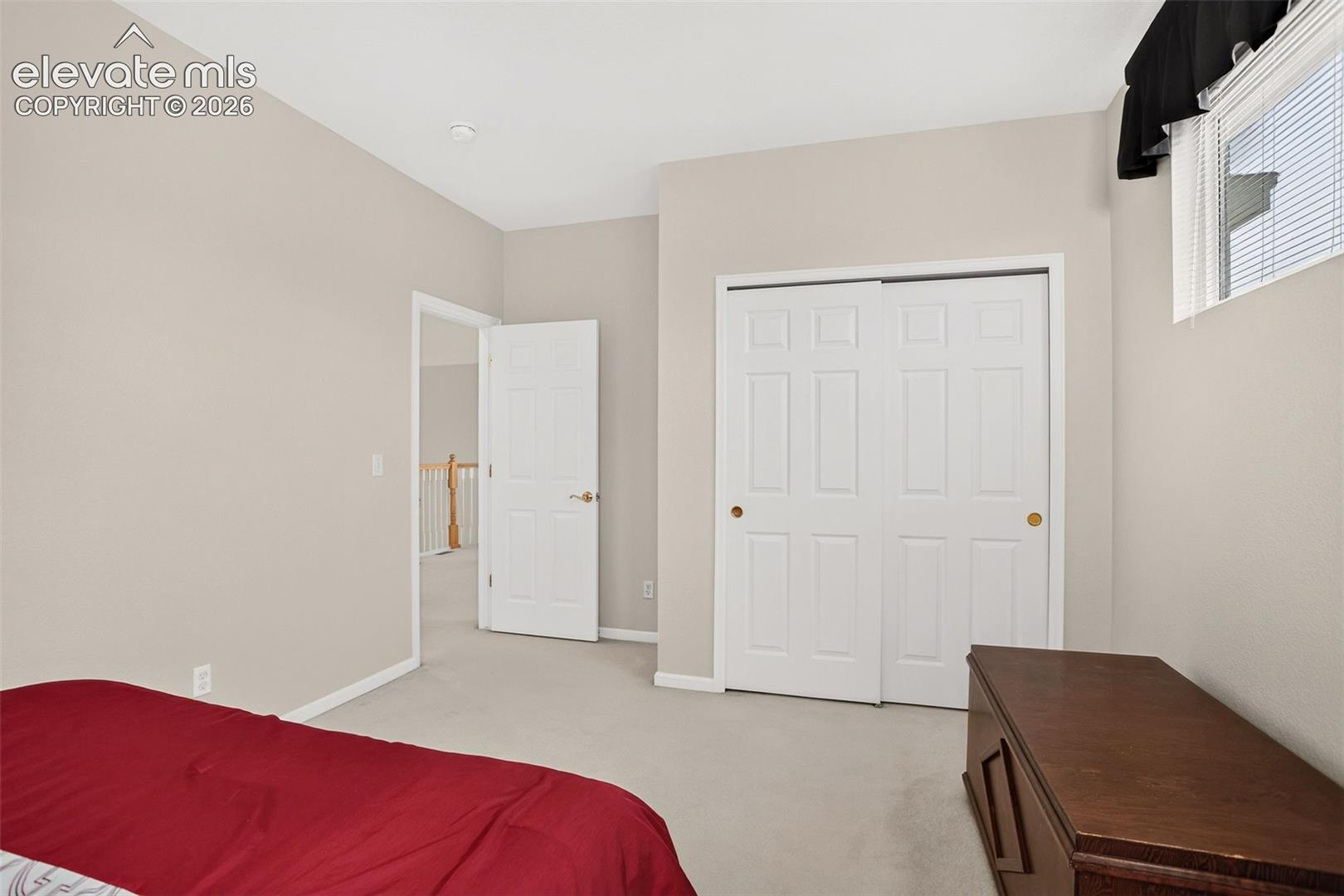 Light-colored wall paint, white trim, carpeted flooring, window with blinds, and a closet with bifold doors