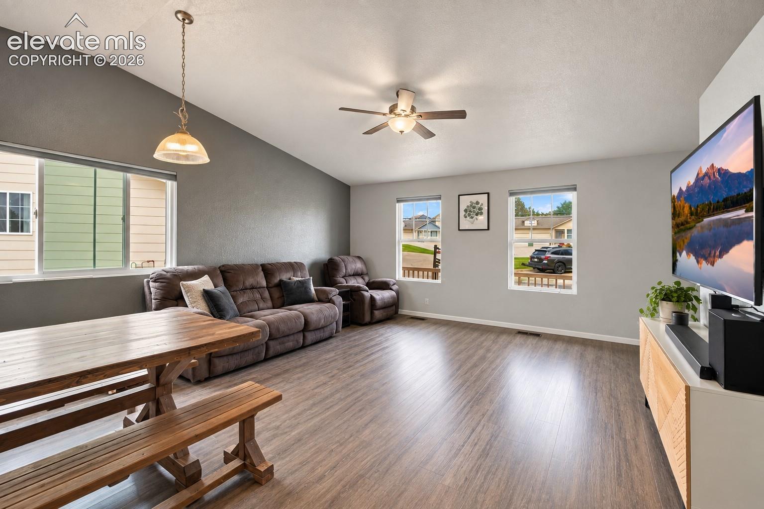 Vaulted ceilings, wood-finish flooring, multiple windows, built-in ceiling fan, and a light fixture