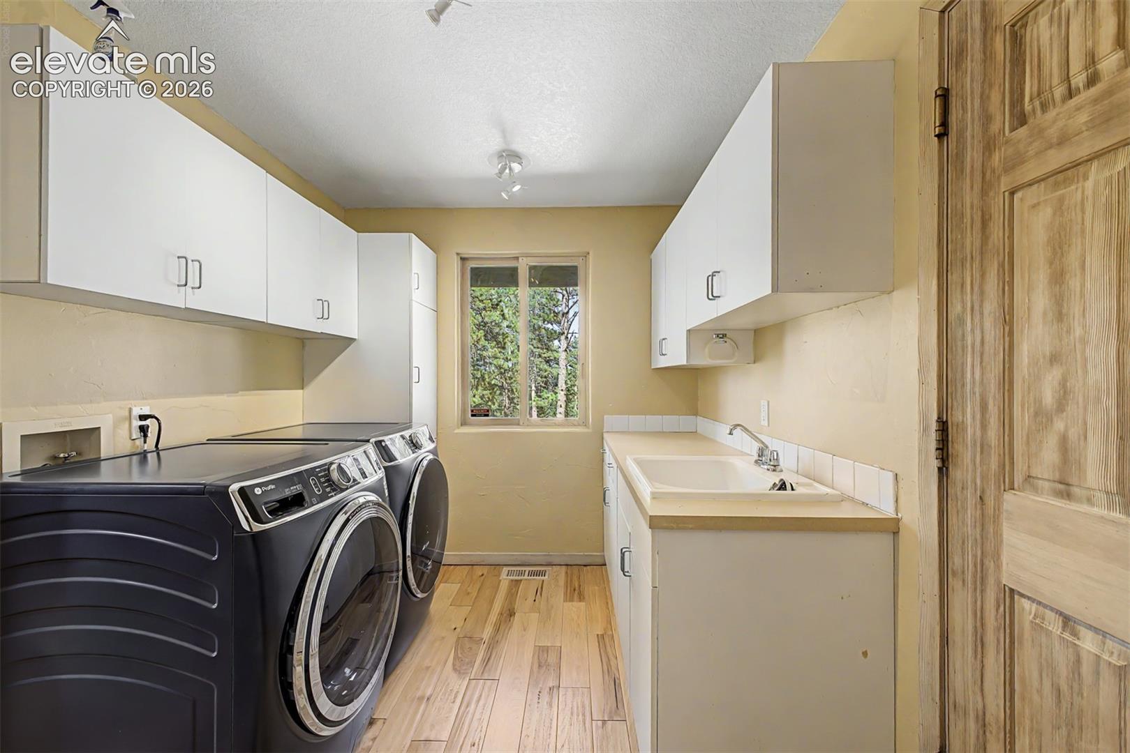 Utility room featuring wood-finish flooring, white cabinetry, a utility sink, and a window